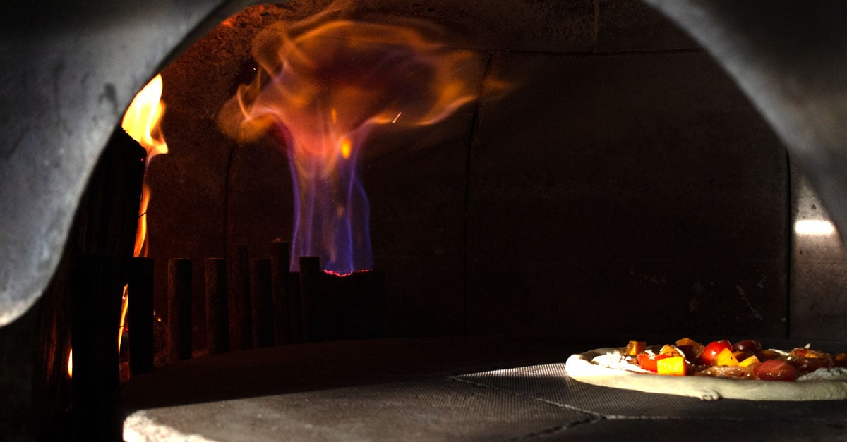 Pizza getting cooked in a pizza oven with huge flames