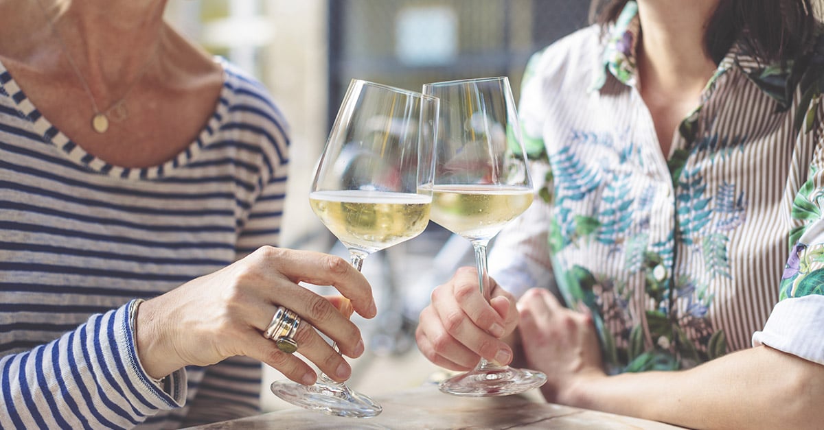 Two women clinking their glasses of white wine together at a restaurant 