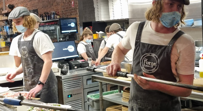 A busy pizza kitchen with digital prep screens