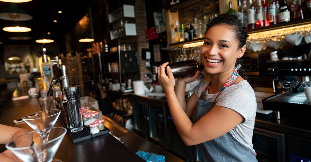 bar tender making a cocktail in a cocktail shaker behind the bar