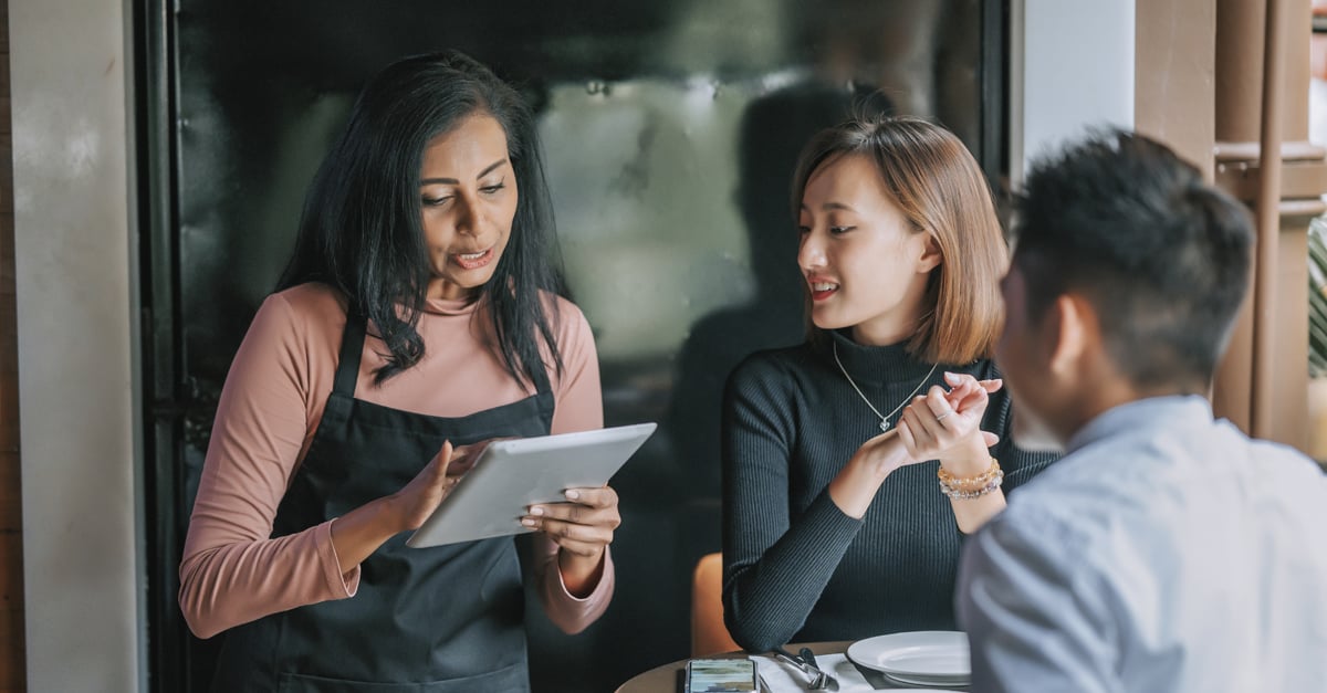 waitress taking customer orders in a restaurant at their table with a hand held tablet