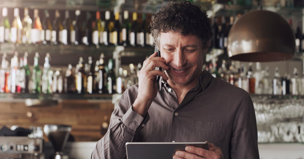 A hospitality operator on the phone whilst also using a POS system in the bar