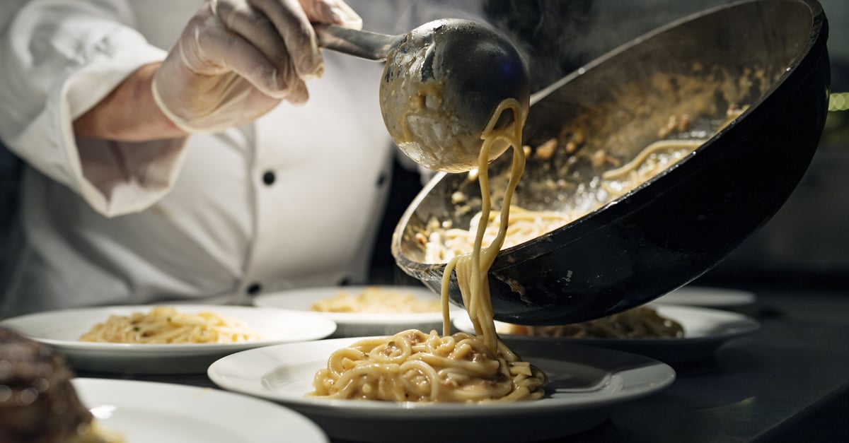 Chef plating up pasta dish onto customers plate 